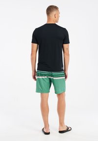 Zwart shirt met korte mouwen, groene zwemshorts met een patroon van horizontale strepen en zwarte slippers. Soepele stof en casual pasvorm.