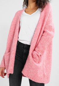 Pink knitted cardigan with an open front, long sleeves, and two front pockets. Made of soft, textured fabric, designed for comfortable layering.