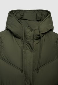 Gilet imbottito verde oliva con collo alto, coulisse e chiusura con bottoni a pressione. Texture liscia con dettaglio di cuciture a forma di diamante.