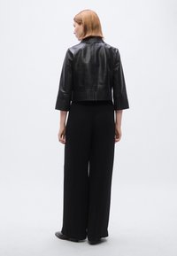 Μαύρο cropped δερμάτινο μπουφάν με μανίκια τριών τετάρτων και ριμπ κάτω όριο, σε συνδυασμό με μαύρο παντελόνι φαρδιάς γραμμής. Απλό, με ματ τελείωμα.