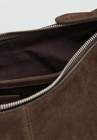 Wnętrze brązowej zamszowej torebki z ciemną, materiałową podszewką, wyposażone w srebrny zamek błyskawiczny i gładką krawędź. Widoczne są minimalne kieszenie.