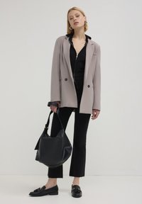 Hellgrauer Blazer, schwarze Zip-Jacke darunter, schwarze ausgestellte Jeans, schwarze Ballerinas mit Hardware-Details und eine schwarze Hobo-Tasche. Glatte Texturen überall.