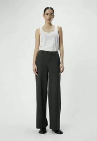 Gray wide-leg trousers made of smooth fabric, featuring a high waist and front pleats, paired with a fitted white tank top. Black shoes are worn.