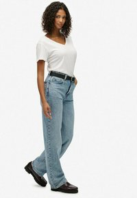 Witte v-hals t-shirt, lichtblauwe rechte jeans, zwarte riem met zilveren gesp, donkere schoenen met een gestructureerde zool. Eenvoudige, casual outfit.