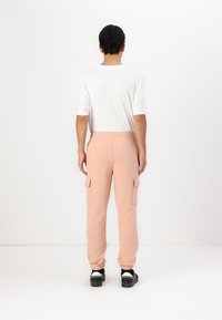 Fersken cargo joggebukser med elastisk midje, sidelommer og smale mansjetter. Brukt med en hvit t-skjorte med korte ermer og svarte sko.