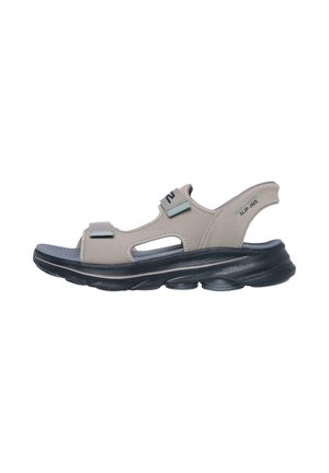 Sandalia beige con puntera abierta, tiras ajustables, suela oscura acolchada y soporte para el talón con la etiqueta "SLIP-INS" diseñada para uso casual.