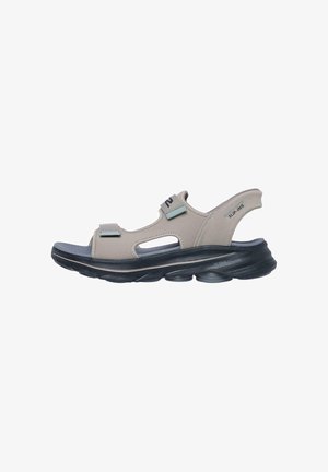 Sandalia beige con puntera abierta, tiras ajustables, suela oscura acolchada y soporte para el talón con la etiqueta "SLIP-INS" diseñada para uso casual.