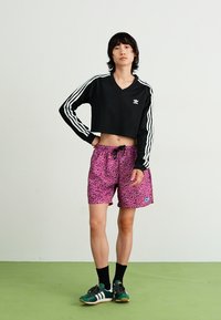 Melna īsā sudraba svītru sporta blūze, apvienota ar rozā leoparda raksta šortiem. Melni sporta zeķes un zaļi sporta apavi papildina šo izskatu.