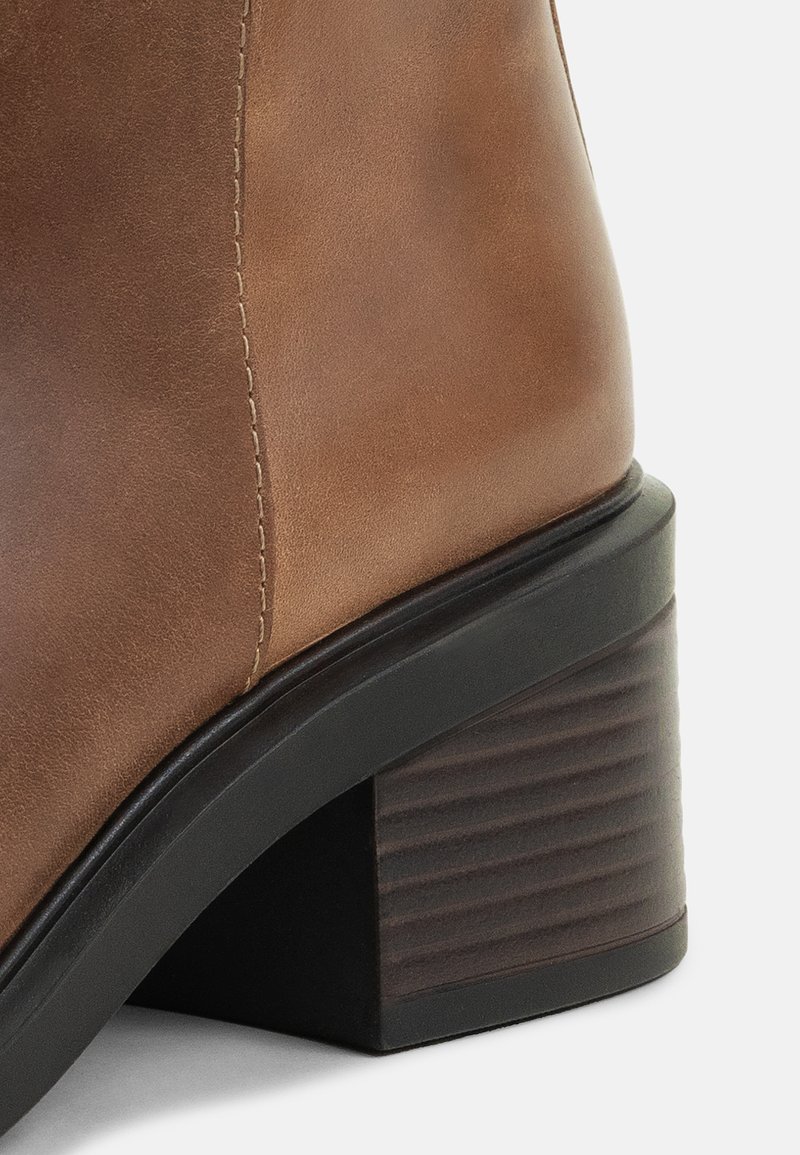 Stivale in pelle marrone alla caviglia con tacco a blocco impilato e scanalature orizzontali, punta arrotondata e dettagli di cucitura a contrasto.