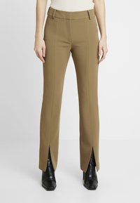 Pantalons marron ajustés avec une taille cintrée, des coutures verticales et des fentes sur les côtés, associés à des bottes à talons noires. Texture de tissu lisse.