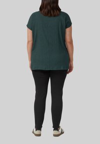 Donkergroene textuurtop met korte mouwen, gecombineerd met zwarte slim-fit broek en lichtgekleurde sneakers met donkere accenten.