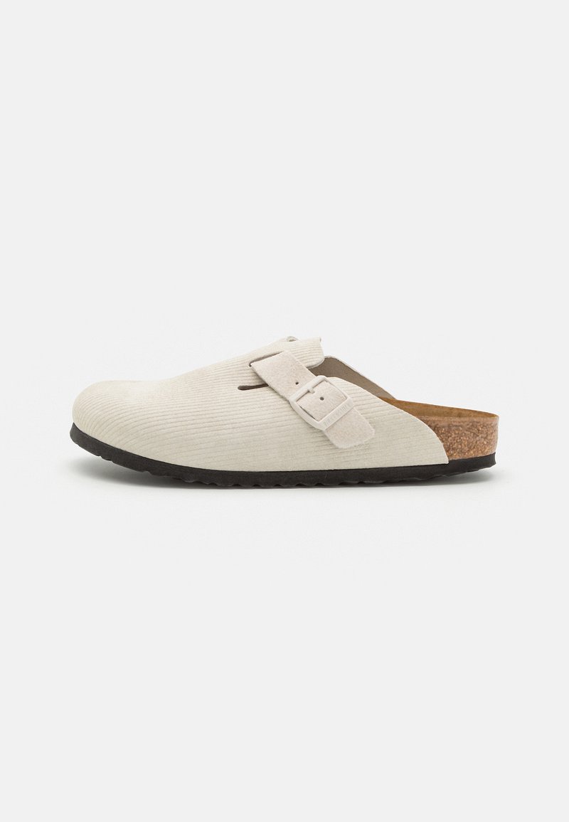 Buty typu chodaki w jasnym beżowym kolorze z korduroyu, z korkową podeszwą środkową i czarną gumową podeszwą. Posiadają jedną regulowaną klamrę.