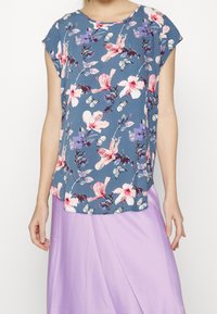 Blå kortärmad topp med blommönster i rosa och lila blommor, kombinerad med en ljuslila kjol, med en avslappnad passform och rund halsringning.