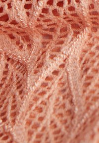 Tissu tricoté en corail clair avec un motif de dentelle ouvert. Design texturé et aéré avec des motifs géométriques complexes et des fibres douces.