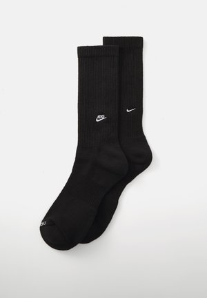 Black ribbed socks made of cotton blend, featuring white Nike logos on the sides and cushioned soles for comfort.