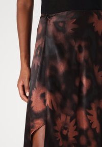 Brun blomstertrykt skjørt med satin tekstur, som har en sideslitt og en knappdetalj i midjen, som skaper en flytende silhuett.