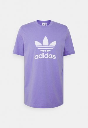 Fioletowa koszulka Adidas z krótkim rękawem, z białym logo trefoil i nazwą marki na przodzie, przedstawiona na jednolitym jasnym tle.