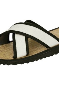 Strappy sandal with black edges, white canvas upper, and a textured natural fiber insole. Features a smooth rubber outsole with scalloped edges.