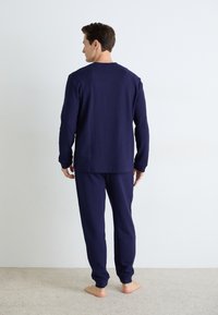 Navy-blaues Waffle-Strick-Loungewear-Set mit langen Ärmeln und Hosen mit gerippten Bündchen, von hinten auf einem beigen Teppich gezeigt.