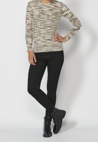 Stickad tröja i ett mjukt, texturerat tyg, med en blandning av beige, krämiga och gråa trådar. Tillsammans med svarta skinny jeans och svarta ankelkängor.