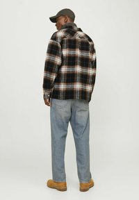 Checkered flannel shirt in black, white, and orange with a collar; paired with light blue denim jeans and tan boots. Simple cap on head.