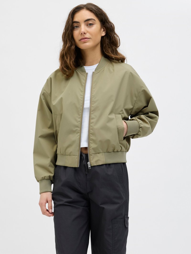 Olive green bomber jacket with a zip front, ribbed cuffs, and hem. Worn over a white top with black cargo pants, smooth fabric texture.
