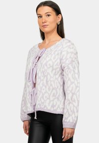 Maglione viola lavorato a maglia con stampa a leopardo, caratterizzato da scollatura a V, chiusure a bow e polsini a coste. Texture morbida e design leggermente cropped.