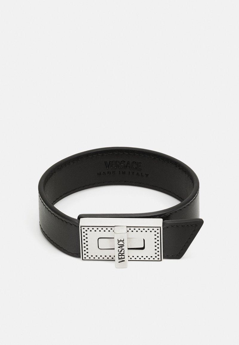 Bracciale in pelle nera con chiusura metallica rettangolare in argento caratterizzata da un design perforato e il logo "VERSACE" in rilievo. Prodotto in Italia.