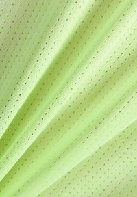 Tissu vert clair avec de petits trous perforés disposés en rangées diagonales, montrant des plis doux et des détails de texture.