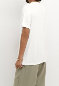 Camiseta blanca de manga corta hecha de algodón suave, con un corte holgado y un escote redondeado, combinada con pantalones verde oliva.