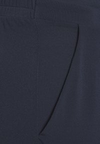 Marineblauer Stoff eines Hosenpaares mit glatter Textur, seitlichem Taschenbereich und elastischem Bund.