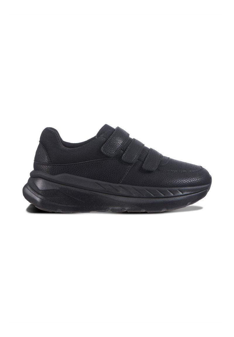 Svart sneaker med två kardborreband, övre del av texturerat tyg, vadderad krage och en kraftig gummisula med ett zigzag-mönster.
