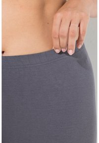 Leggings de algodón gris con una cintura lisa, que presentan una textura suave y un diseño ajustado, mostrados parcialmente con una mano ajustando la cintura.