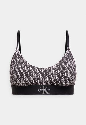Black bralette made of smooth fabric, featuring a repeating white logo pattern and a black logo band at the bottom. Adjustable straps.