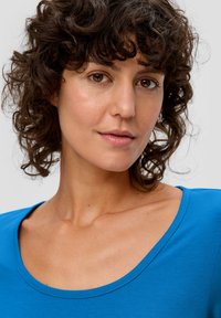 Blaues kurzärmliges Oberteil mit Rundhalsausschnitt, weichem Stoff und figurbetontem Schnitt. Verfügt über eine glatte, einheitliche Farbe mit subtilen Nähdetails.