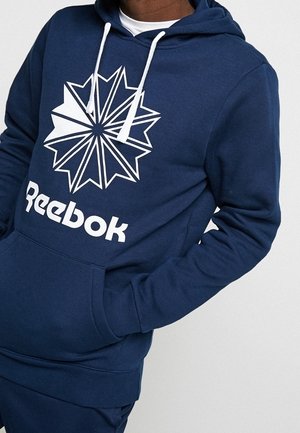 Haut à capuche bleu marine en tissu doux ; présente un grand logo étoile géométrique blanc et le texte "Reebok" sur le devant ; capuche à cordon réglable.