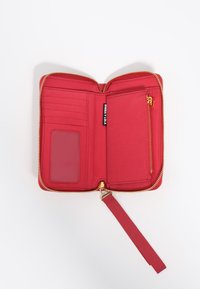 Cartera roja con cremallera que cuenta con slots para tarjetas, un soporte transparente para identificación y un cierre dorado. Incluye una correa de muñeca de tela a juego.