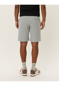 Grå shorts med teksturert overflate, utstyrt med to baklommer. Kombinert med mønstrede sokker og joggesko, fotografert fra baksiden.