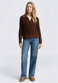 Brązowy pulower o fakturze z dekoltem w serek i kontrastującym kołnierzem, zestawiony z jasnobłękitnymi prostymi jeansami i brązowymi zamszowymi butami.