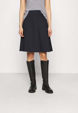 Woman wearing navy A-line skirt, black knee-high boots, and a tucked-in short-sleeve white shirt with black horizontal stripes.