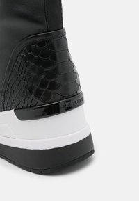 Sneaker nera con un motivo a pelle di serpente testurizzato, dettagli lucidi e una suola intermedia bianca con una suola in gomma nera.