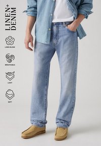 Lyseblå linblandingsjeans med avslappet passform og myk tekstur, kombinert med brune mokkasinsko og en lyseblå skjorte.