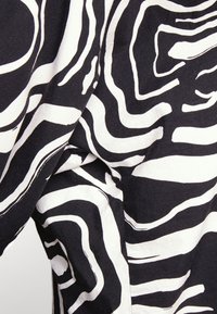 Tessuto in bianco e nero con linee ondulate audaci che creano un motivo astratto. La trama sembra morbida e leggermente pesante.