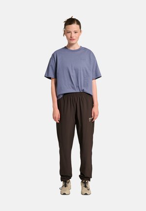 Overmaat blauwe katoenen T-shirt met korte mouwen, gecombineerd met zwarte baggy sweatpants met een gouden logo. Beige sneakers maken de outfit compleet.