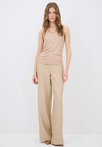Lysbeige tanktop med en struktureret overflade, parret med bredbenede beige stribede bukser, der har lodrette hvide striber. Neutrale nuancer.