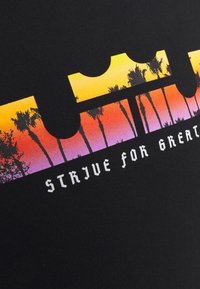 Camiseta de tela negra con un diseño gráfico que presenta un degradado de atardecer en tonos de naranja, rosa y púrpura, acentuado por siluetas de palmeras y texto.