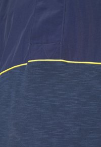 Tmavě modrý top s krátkými rukávy a texturovaným hladkým povrchem, zdobený žlutým páskem na spodním lemu a prošitým detailem na látce.