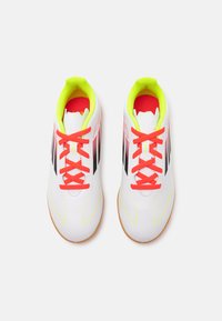 Scarpette da calcio bianche con accenti giallo brillante e lacci rossi. Presentano strisce nere sui lati e una suola in gomma testurizzata.