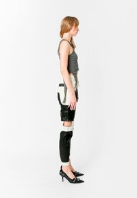 Pantalones de cuero con parches en negro y crema con recortes, combinados con una camiseta gris ajustada y zapatos de tacón negro puntiagudos.