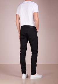 Black jeans with a slim fit, cotton material, back pockets, and a small tag. Paired with a plain white short-sleeve t-shirt and white sneakers.